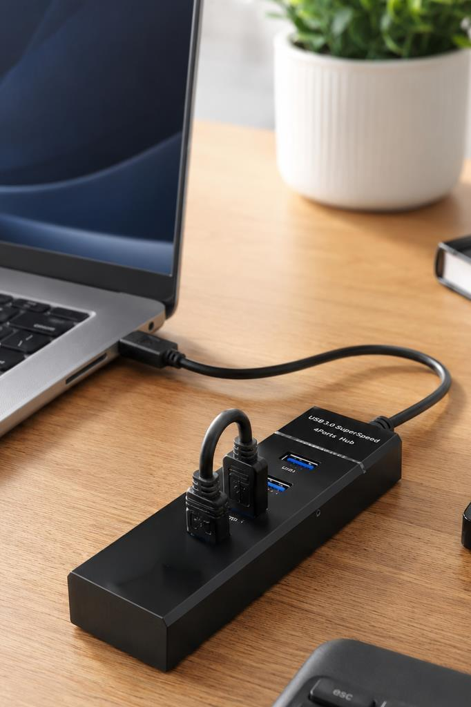 Bağlı iki cihazı olan siyah bir USB hub, dizüstü bilgisayarın yanında ahşap bir masanın üzerinde duruyor.