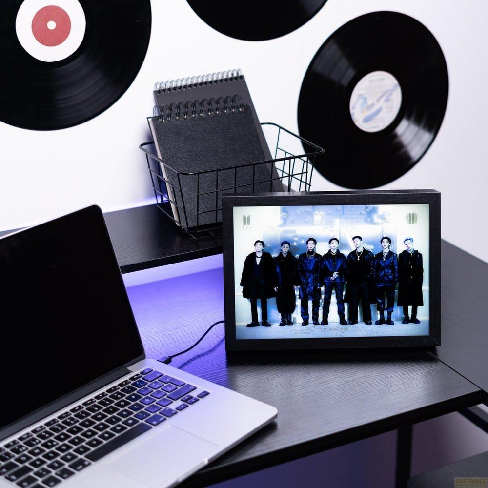 Ein Laptop steht neben einem digitalen Bilderrahmen mit sieben jungen Männern, umgeben von Schallplatten.