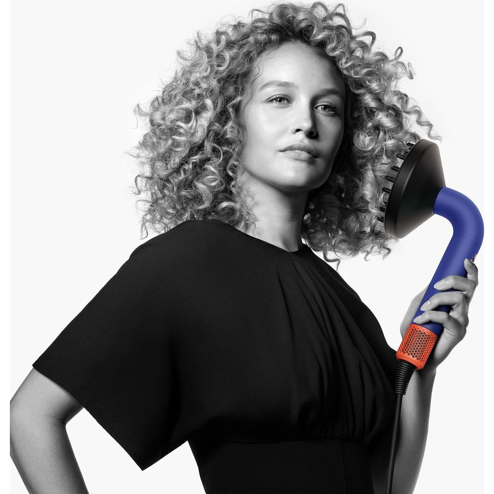 Donna con capelli ricci tiene un diffusore blu per asciugacapelli.