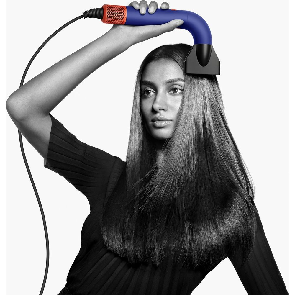 Una donna asciuga i suoi lunghi capelli lisci con un asciugacapelli blu e arancione.