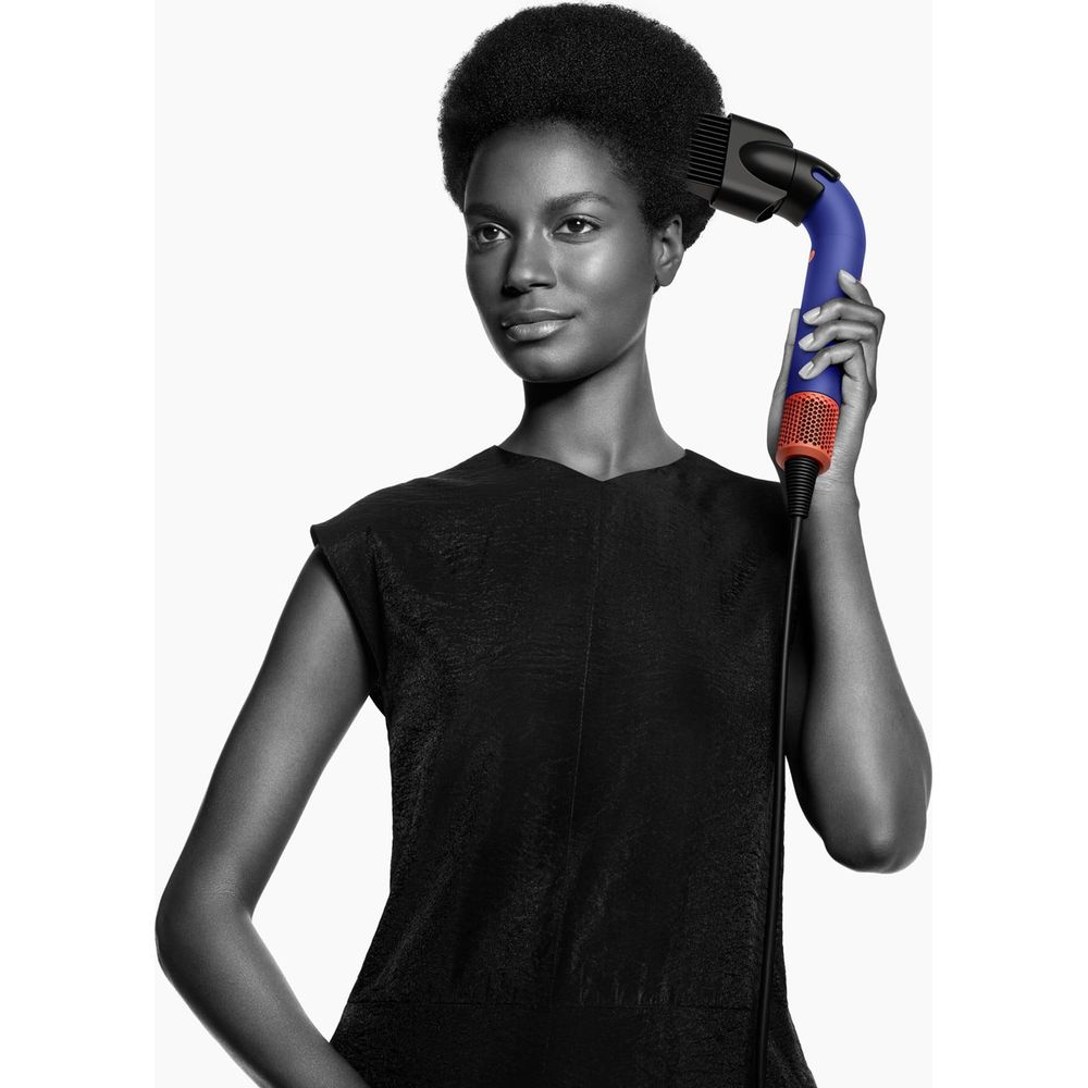 Donna con afro asciuga i capelli con asciugacapelli blu e rosso.