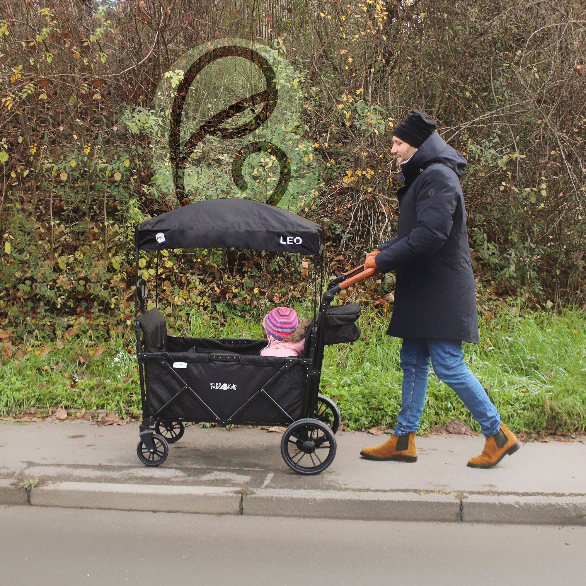 Mann schiebt Kinderwagen mit Kind auf einem Gehweg neben Büschen.