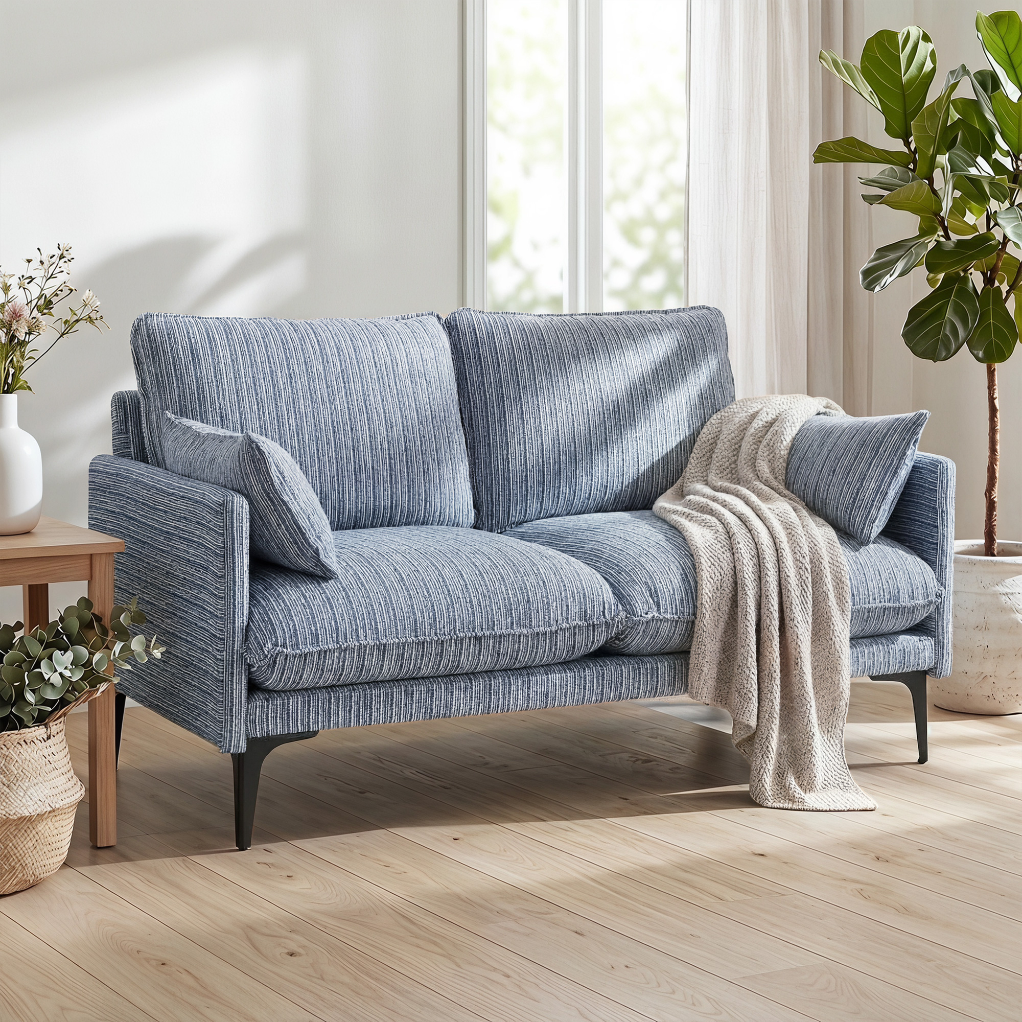 Un divano a righe blu con cuscini e coperta, accanto a un tavolo di legno e una pianta.