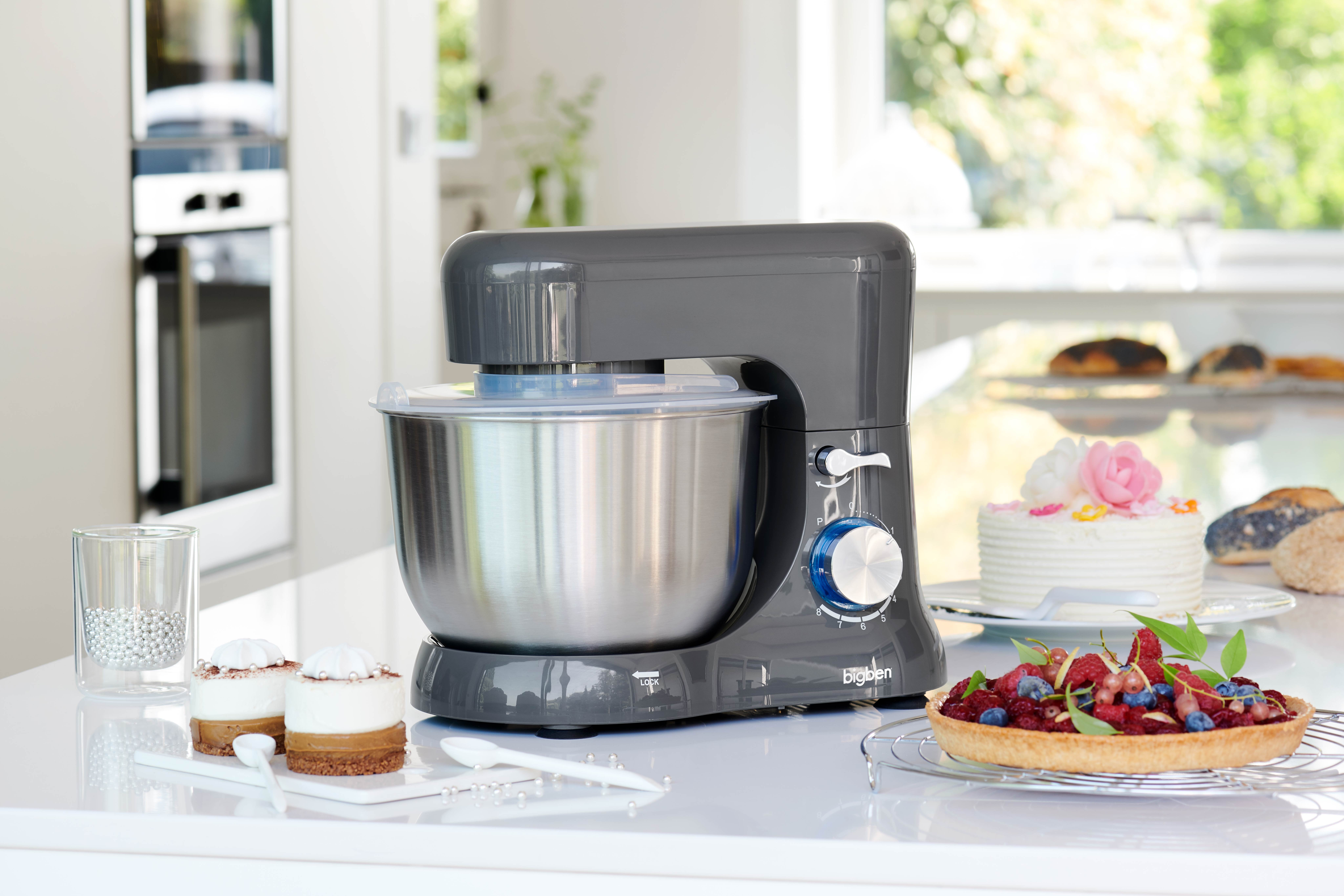 Un robot da cucina grigio su un piano di lavoro con torte e pasticcini.