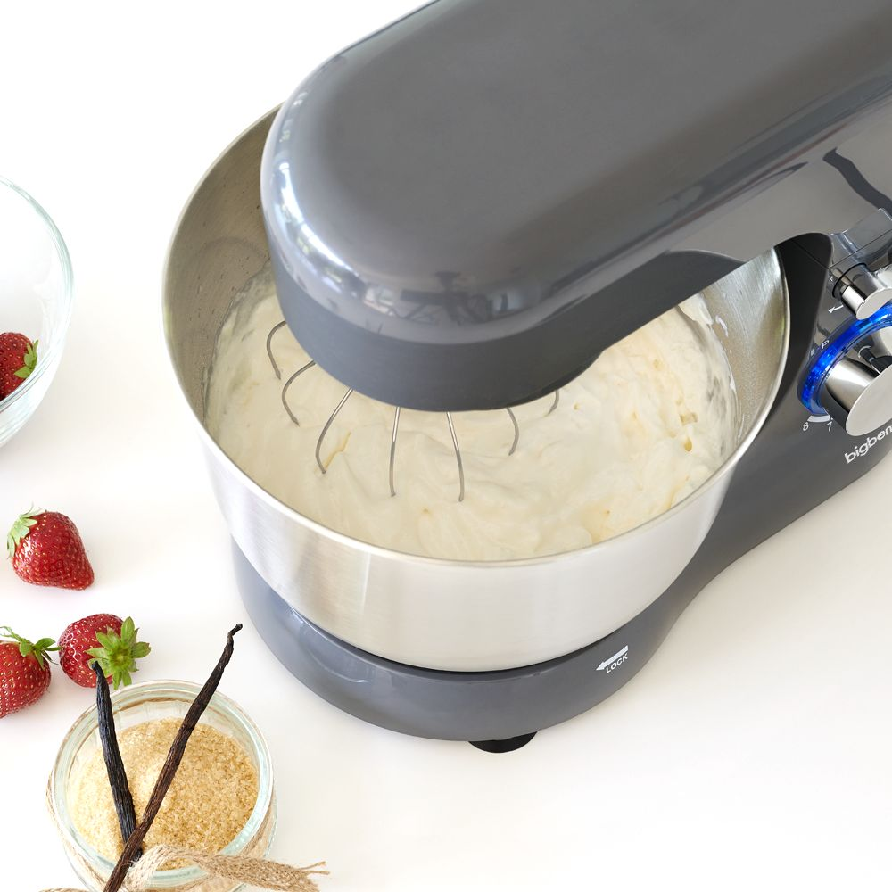 Impastatrice grigia con frusta che monta la panna. Fragole e bacche di vaniglia vicine.