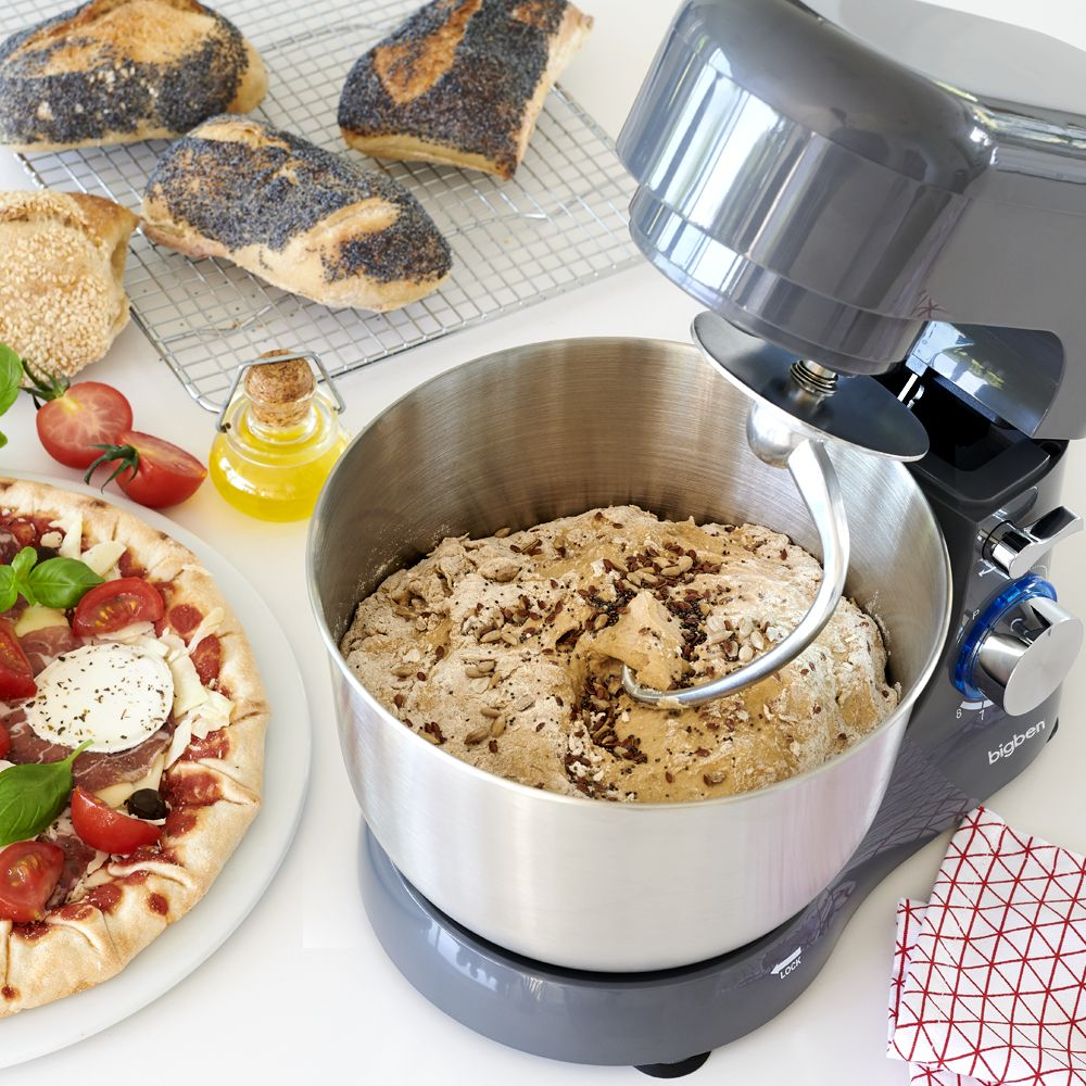 Un robot da cucina con impasto in una ciotola, accanto a pane, pomodori e pizza.