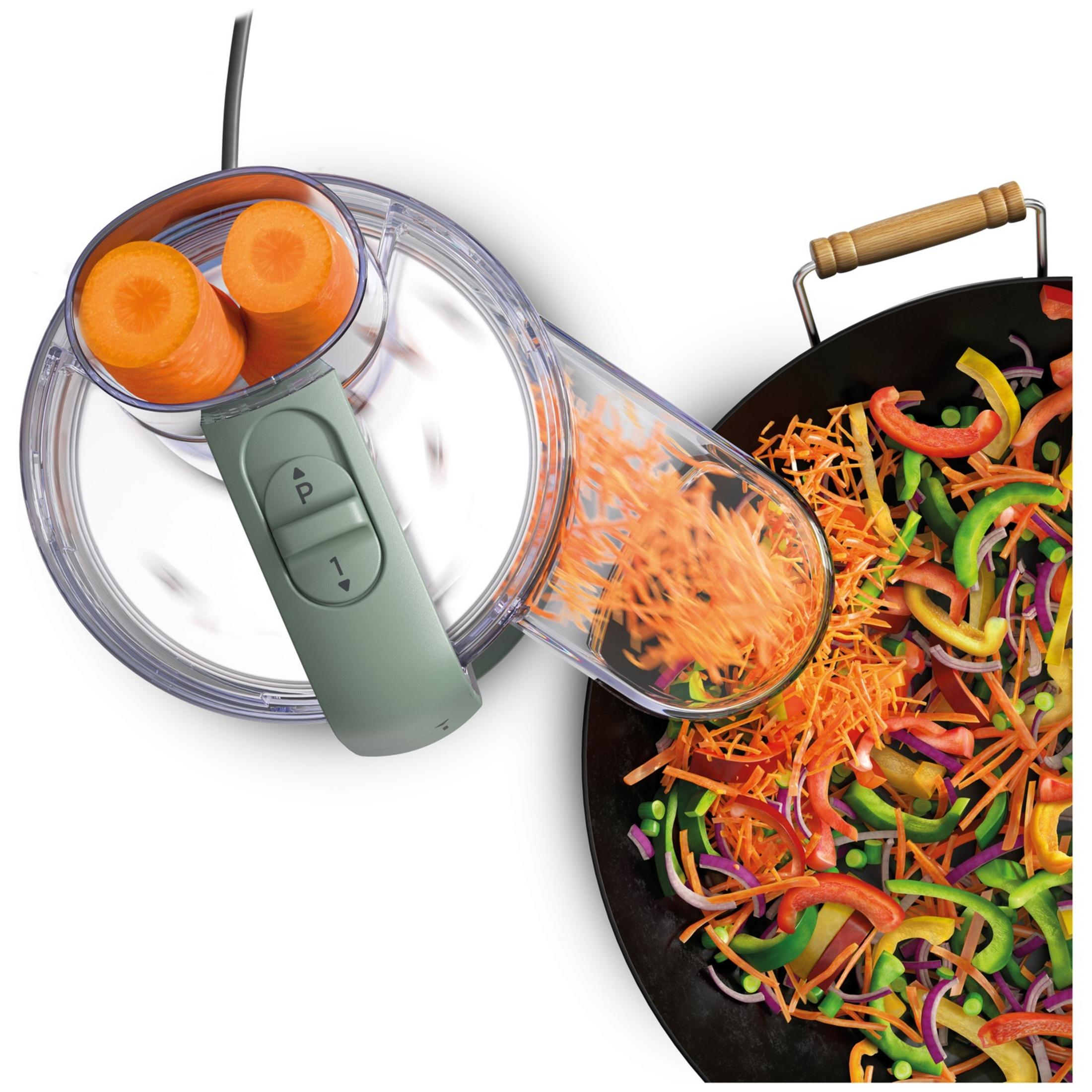 Carote grattugiate da un robot da cucina in un wok pieno di verdure tritate.