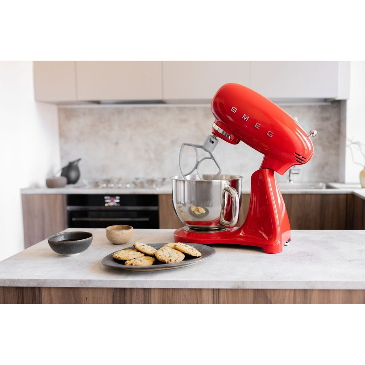Un robot da cucina SMEG rosso è su un bancone accanto a una ciotola di biscotti.