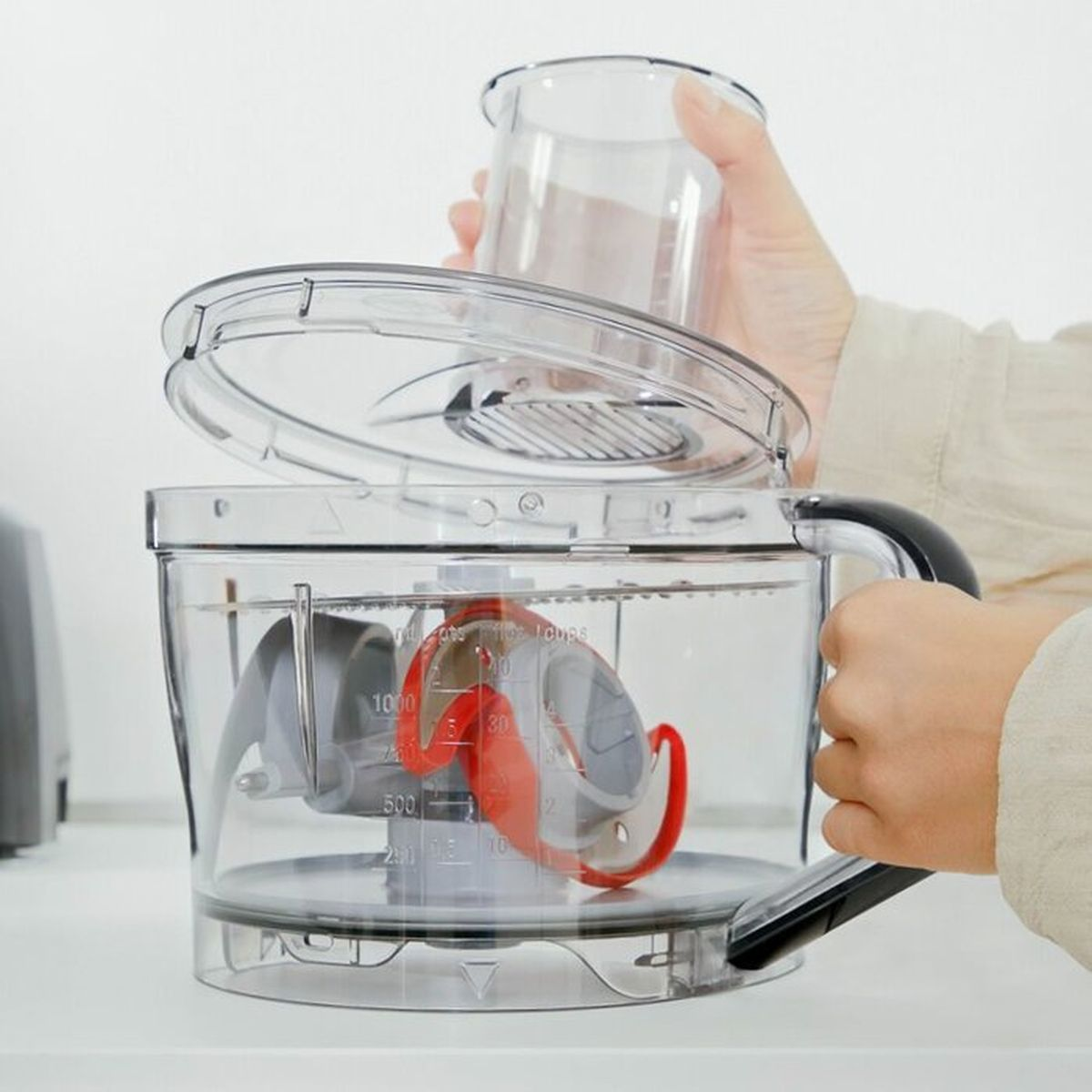 Una mano appoggia un coperchio trasparente sulla ciotola di un robot da cucina con lame.