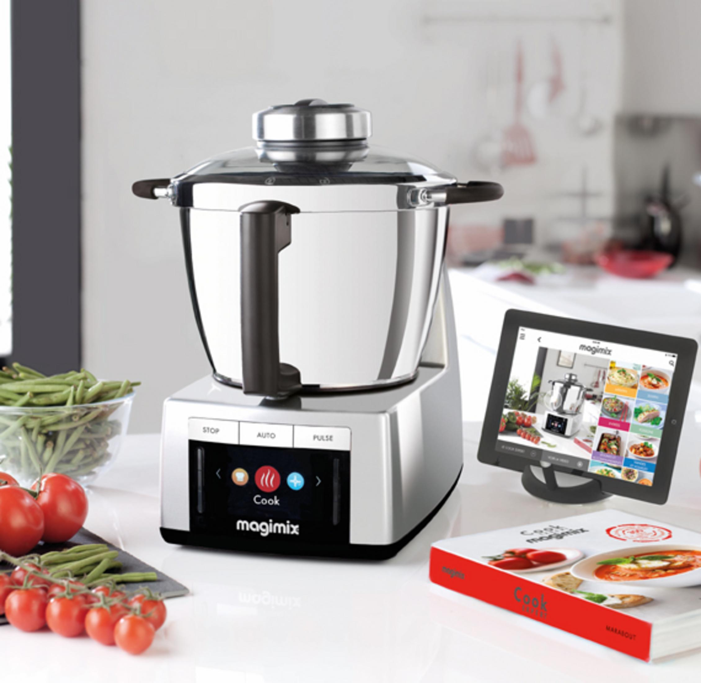 Un robot da cucina Magimix con tablet e libro di cucina, accanto a pomodori freschi e fagiolini.