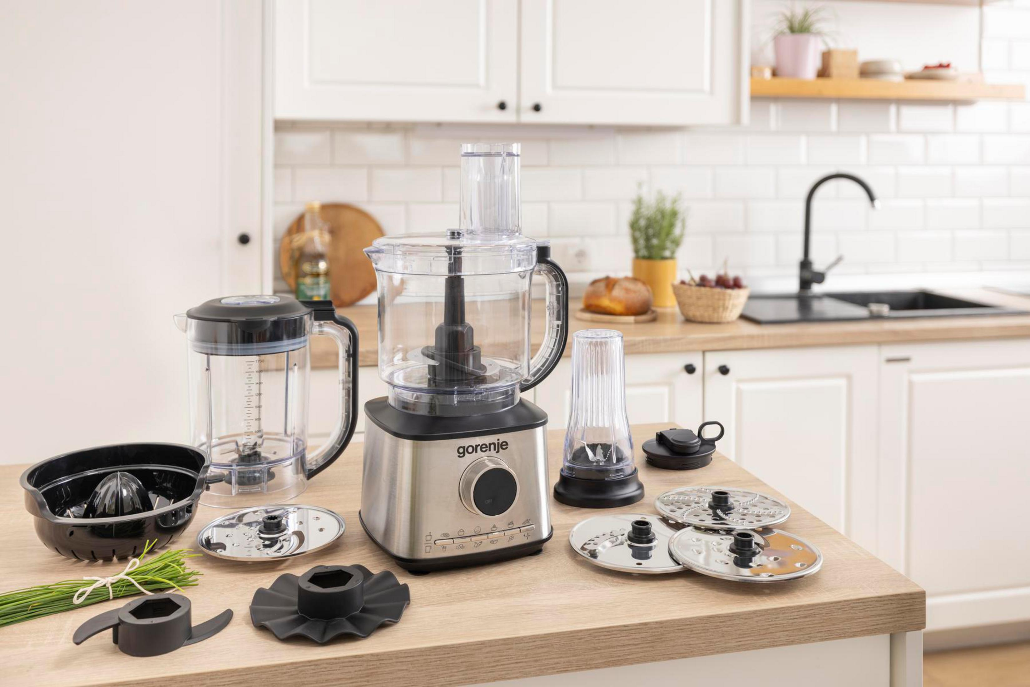 Robot da cucina con accessori: ciotola, frullatore, dischi e paraspruzzi sul piano.