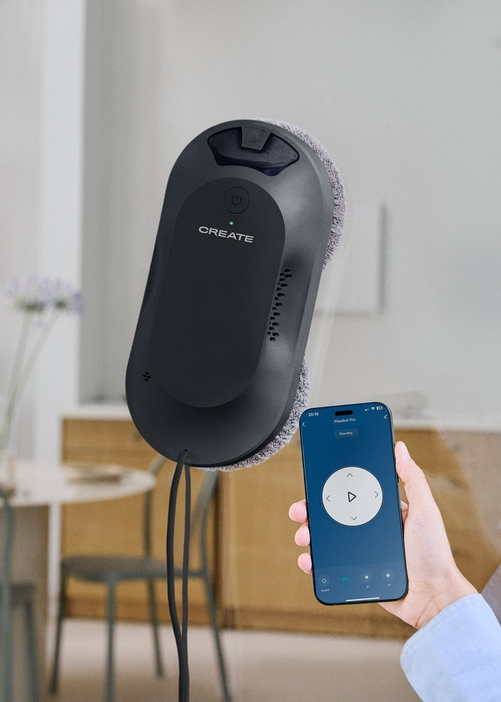 Un robot lavavetri nero aderisce a una finestra, con una mano che tiene uno smartphone nelle vicinanze.