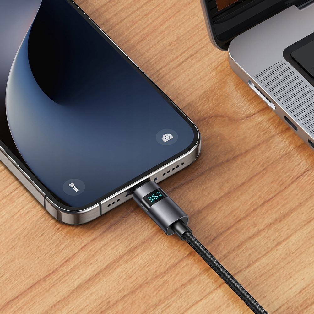 Ahşap bir masada bir dizüstü bilgisayara bağlı USB-C kablosuyla bir telefon şarj oluyor.