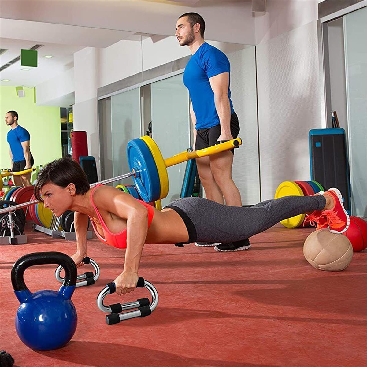 Frau macht Liegestütze auf Griffen, Mann hebt Hantel, Fitnessstudio.