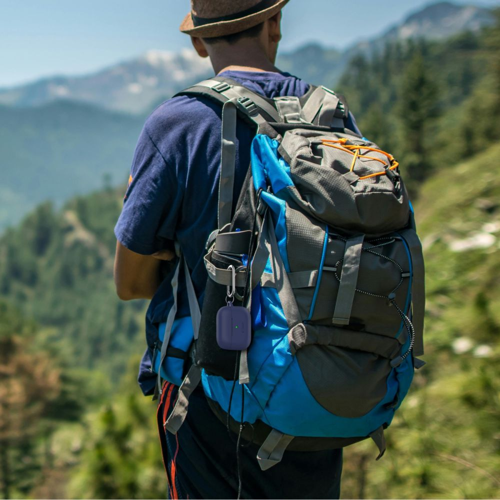 A man hikes in the mountains with a backpack and a purple case attached.