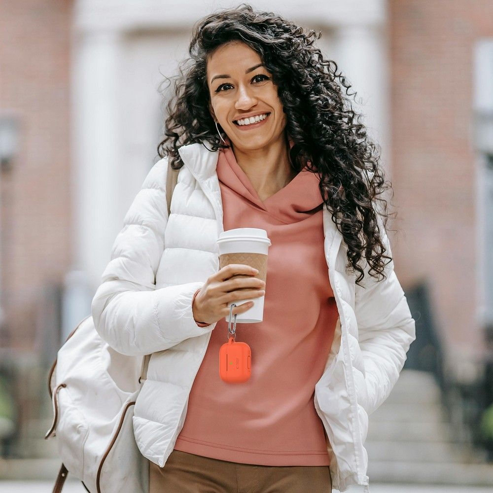 A woman with curly hair holds a coffee cup and wears a white jacket.