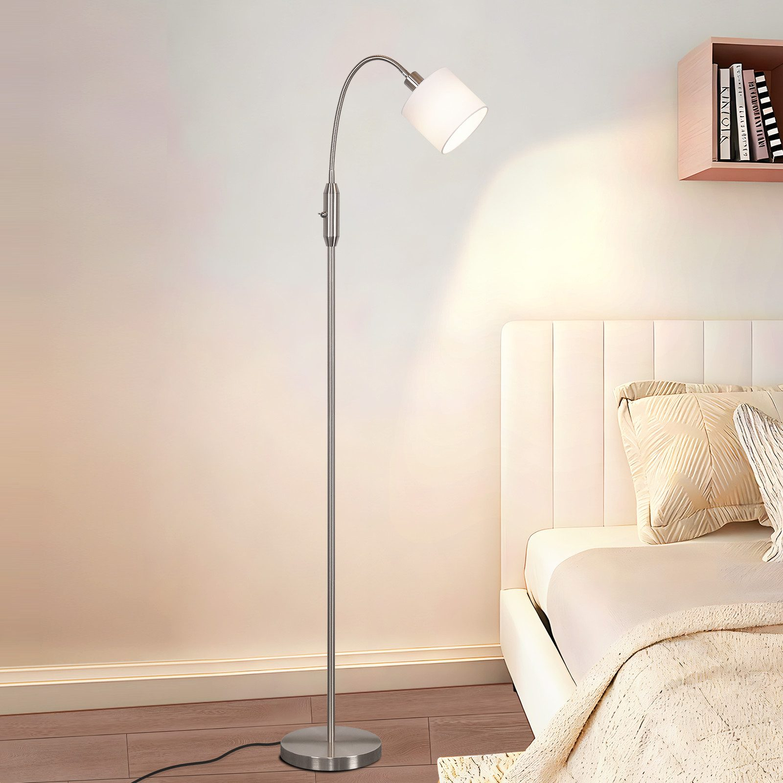 Una moderna lampada da terra argentata accanto a un letto con cuscini bianchi.