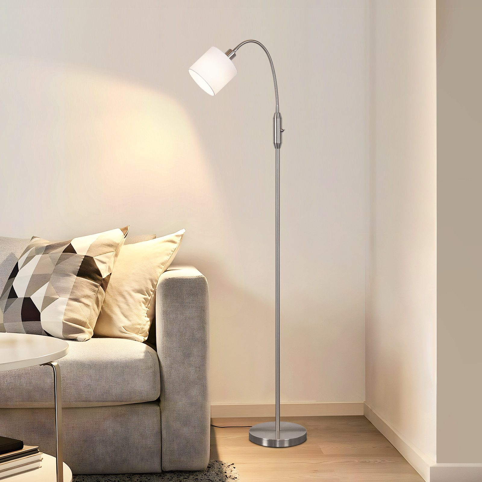 Una lampada da terra moderna accanto a un divano con cuscini, illuminata.
