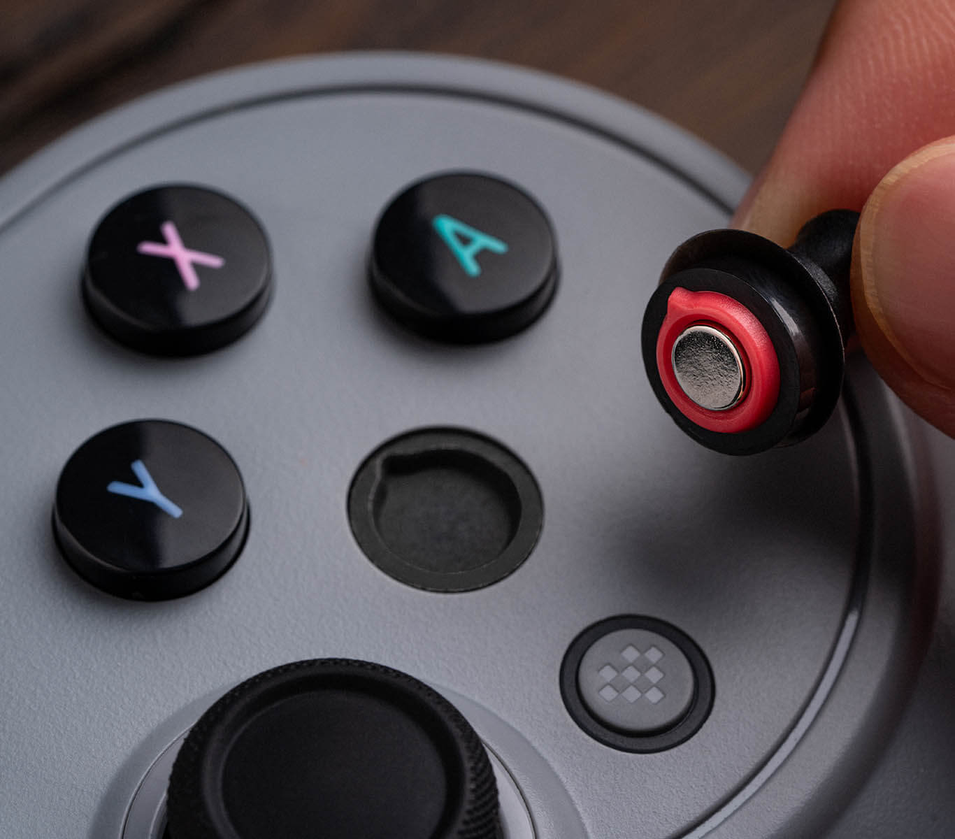 Dłoń trzyma nakładkę na joystick z czerwonym brzegiem nad szarym kontrolerem.