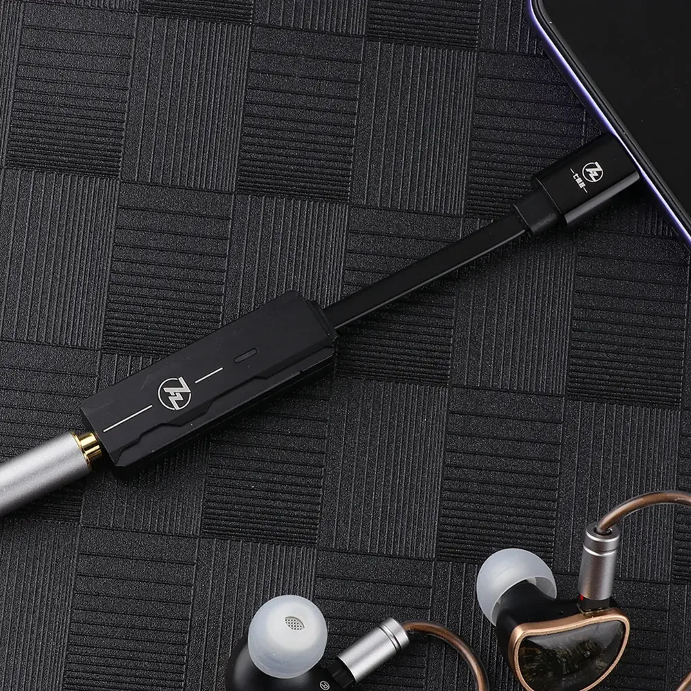 Siyah USB-C adaptör, telefonu gümüş ve altın ses jaklı kulaklıklara bağlar.