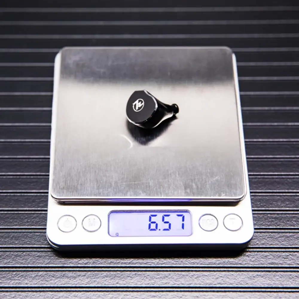 Beyaz logolu siyah nesne dijital tartıda. Ağırlık 6,57g.