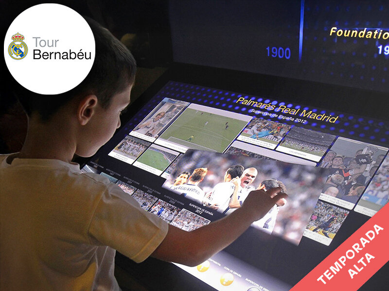Niño toca pantalla interactiva con imágenes de futbolistas en el museo del Bernabéu.