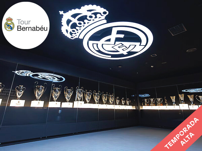 Sala de trofeos con muchas copas en vitrinas, logo del Real Madrid arriba.