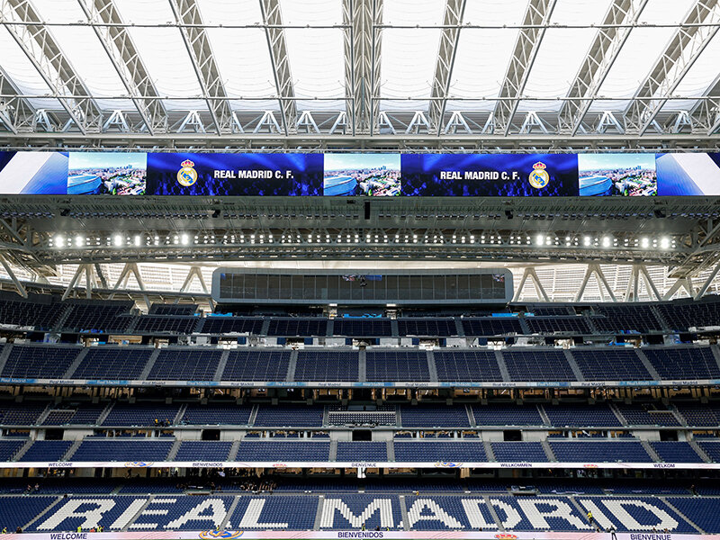 Asientos vacíos del estadio bajo una pantalla gigante que muestra 'REAL MADRID C. F.'