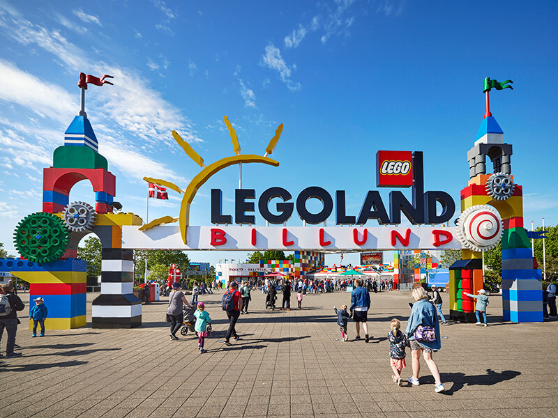 La puerta de LEGOLAND Billund con coloridas torres de Lego y muchos visitantes al sol.