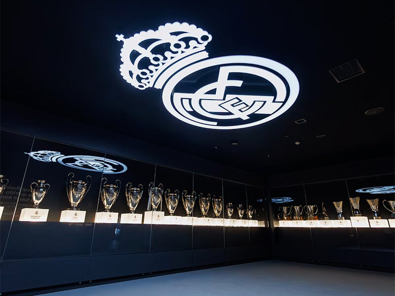 Una fila de trofeos expuestos en una vitrina oscura, con un logo en el techo.