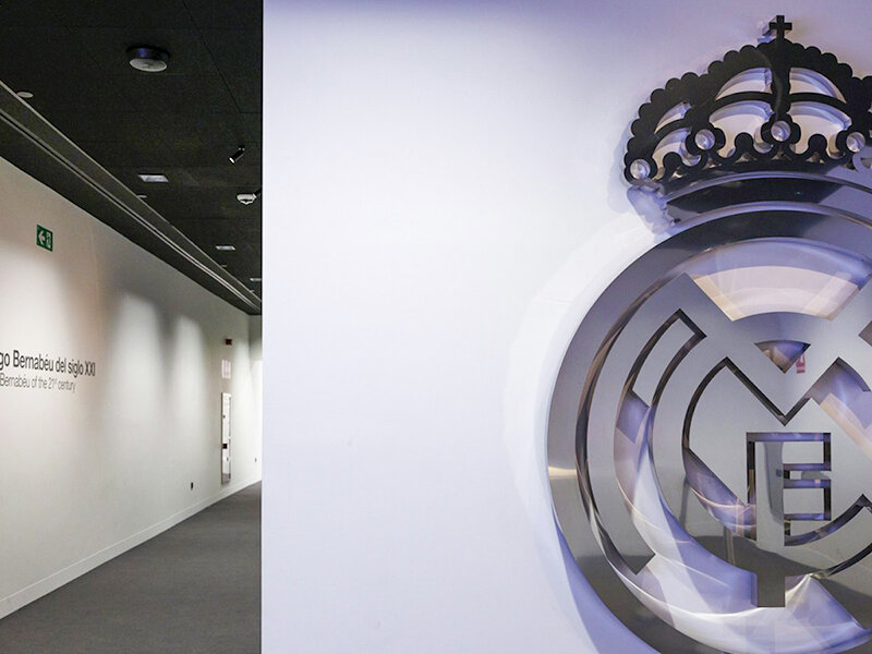 Gran emblema plateado con corona y letras MCM en pared blanca.