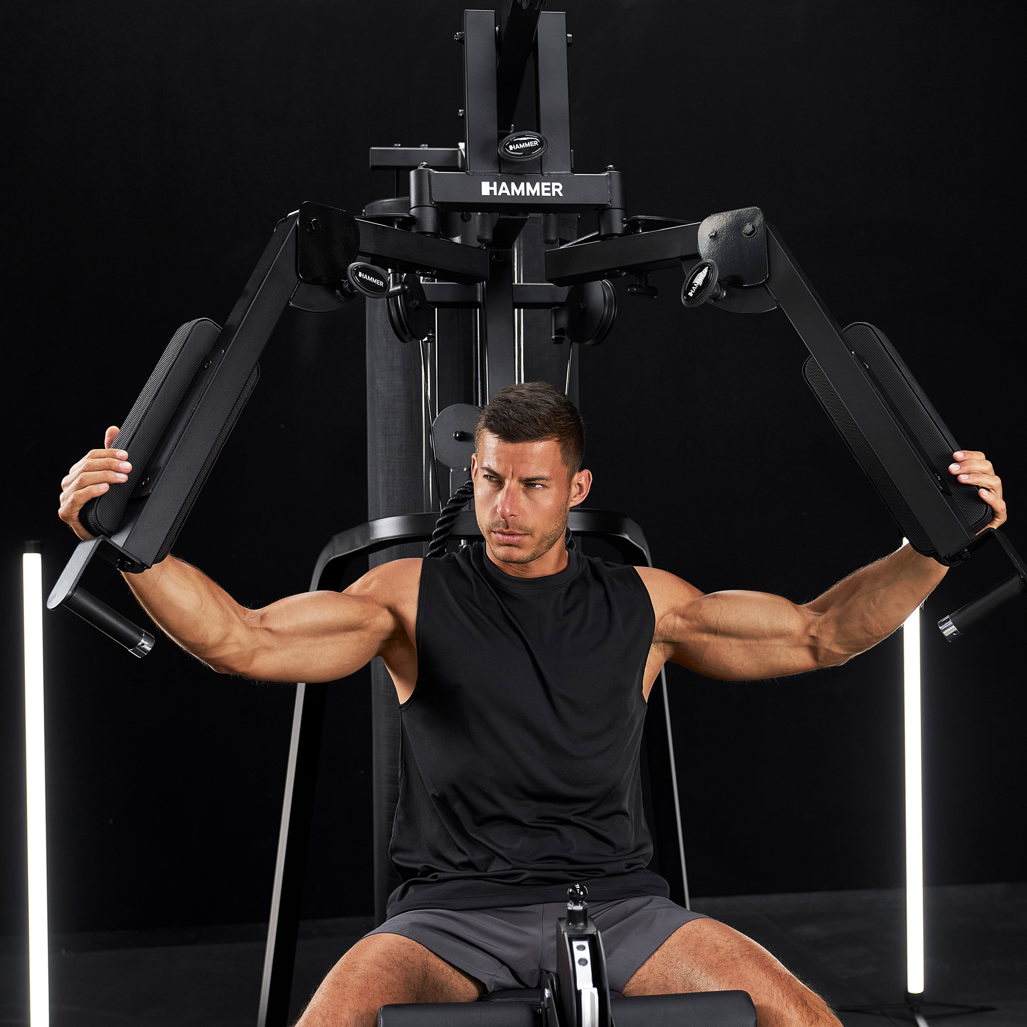 Ein muskulöser Mann trainiert an einem schwarzen Fitnessgerät mit Kabelzug.