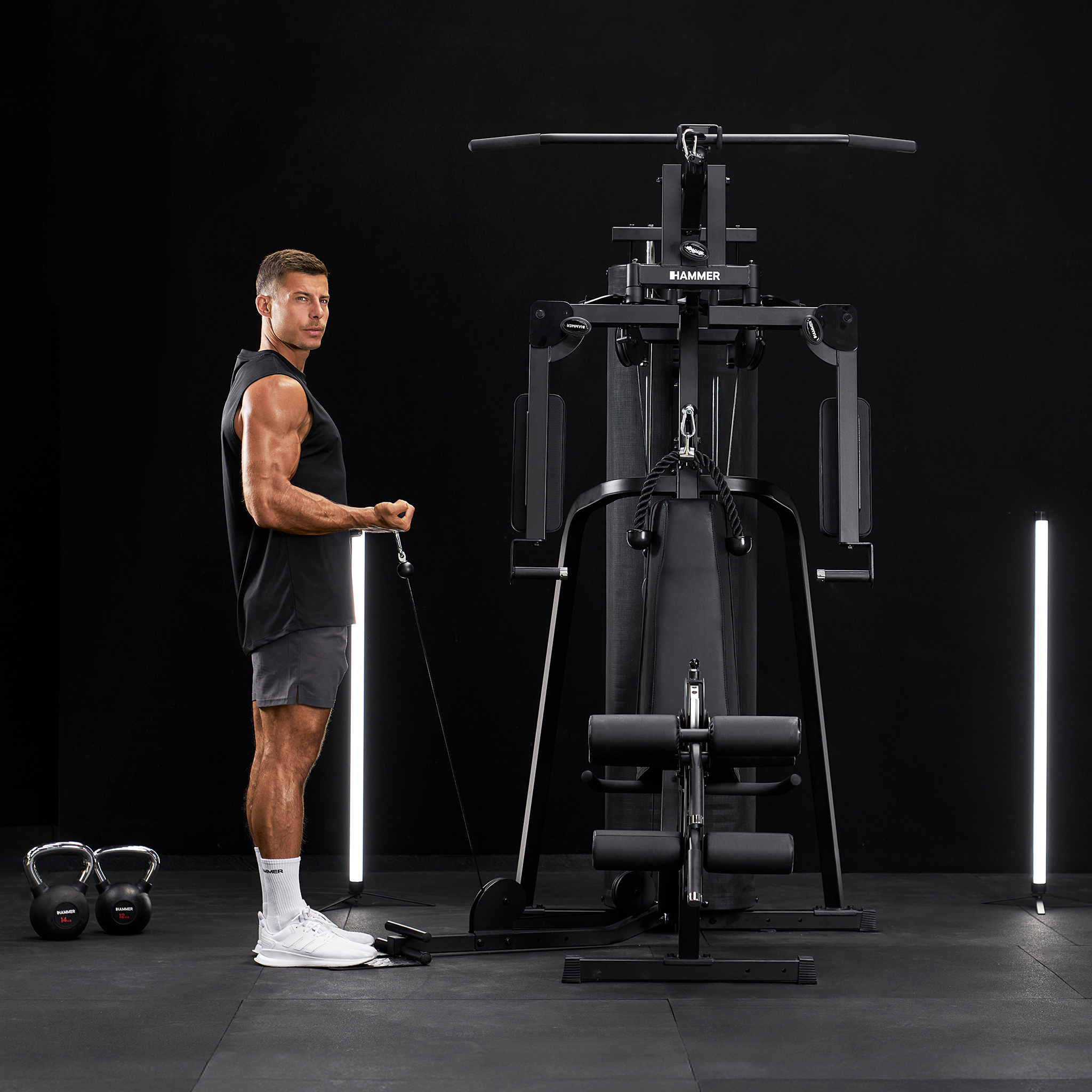 Ein Mann trainiert mit einem Kabelzug an einem Fitnessgerät vor schwarzem Hintergrund.