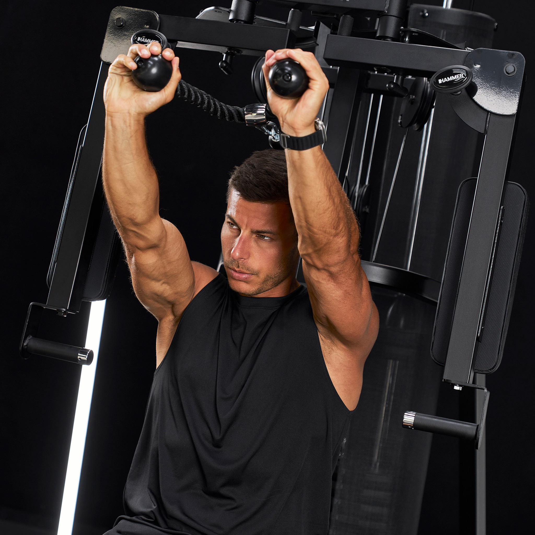 Ein muskulöser Mann trainiert an einem schwarzen Fitnessgerät mit Kabelzug.