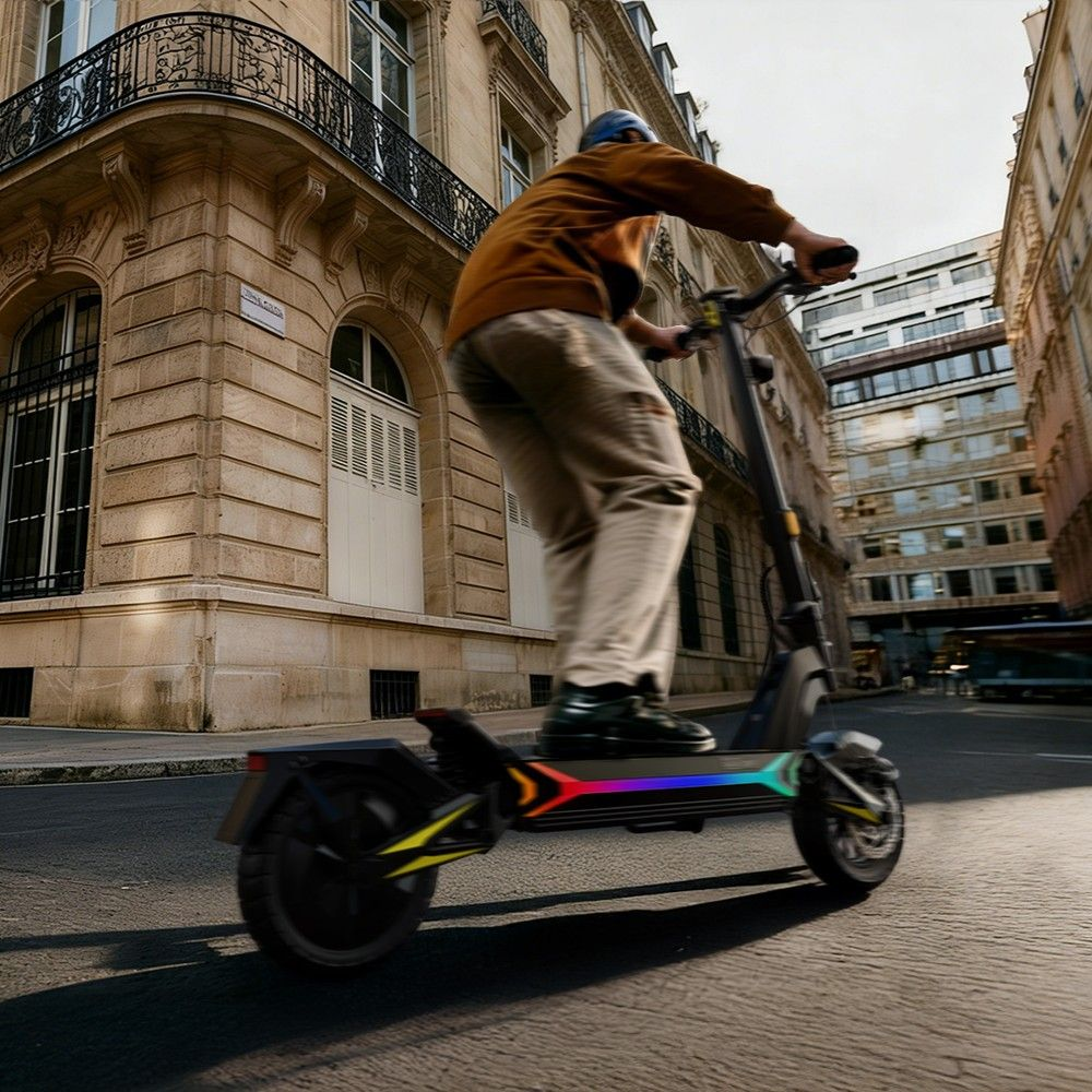 Uomo guida uno scooter elettrico in una strada cittadina con luci colorate.