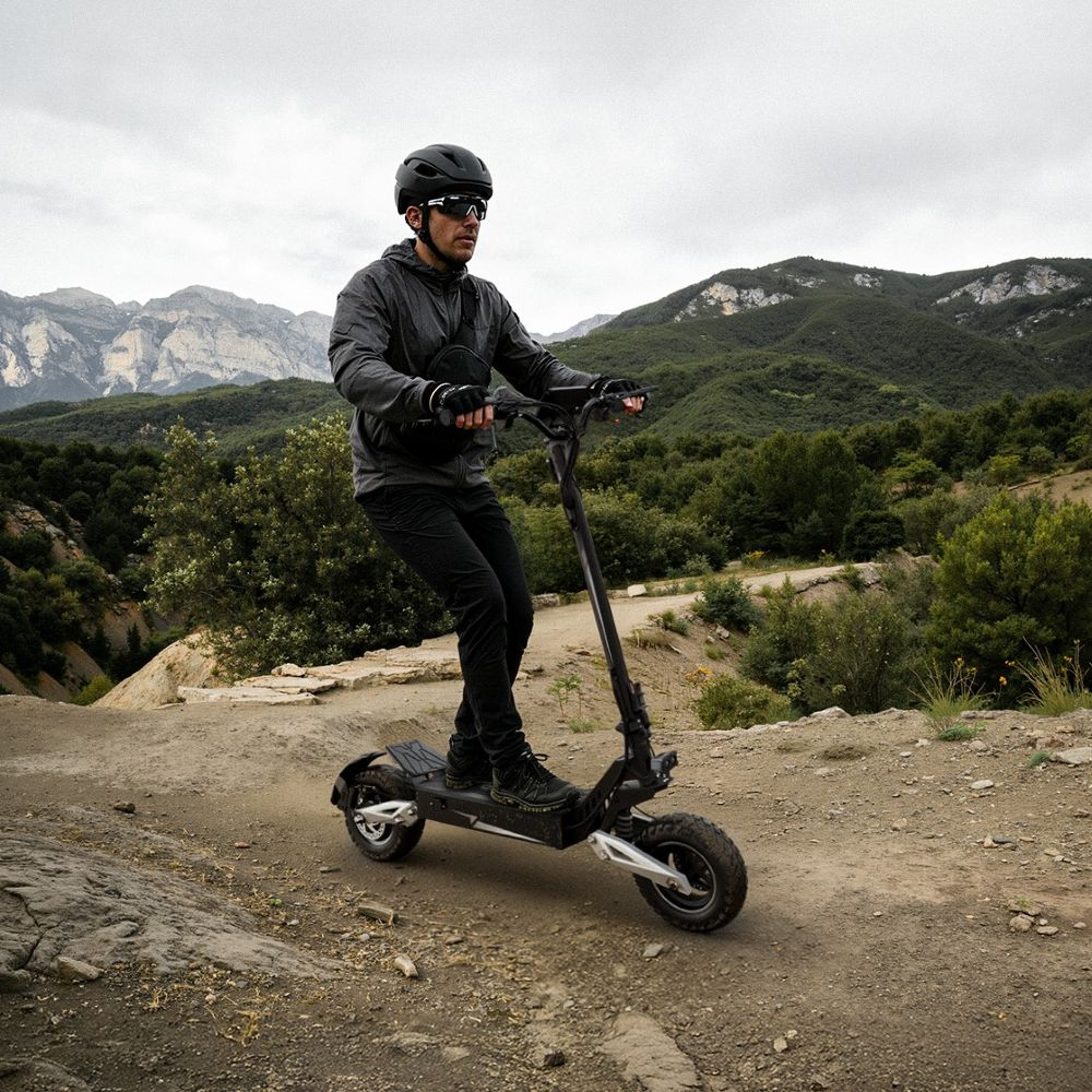 Un uomo guida un monopattino elettrico su un sentiero sterrato in montagna.
