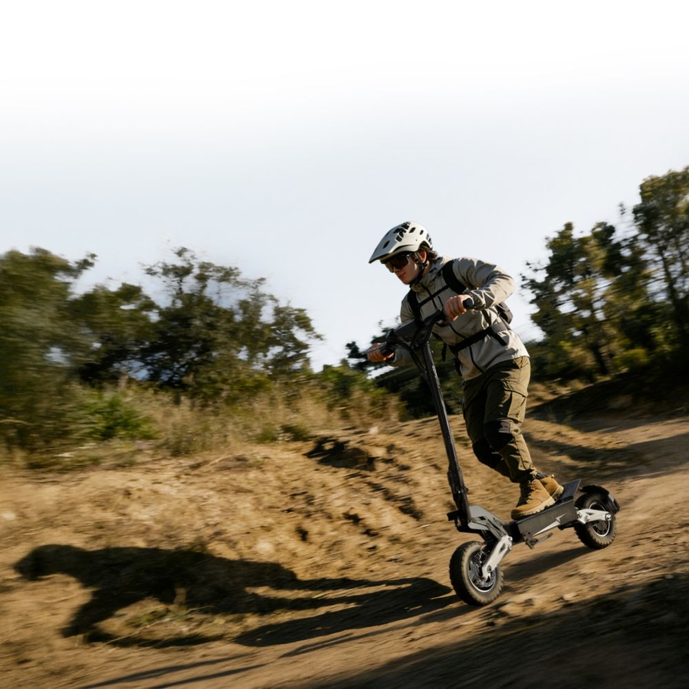 Uomo con casco guida scooter elettrico su sentiero sterrato con alberi.