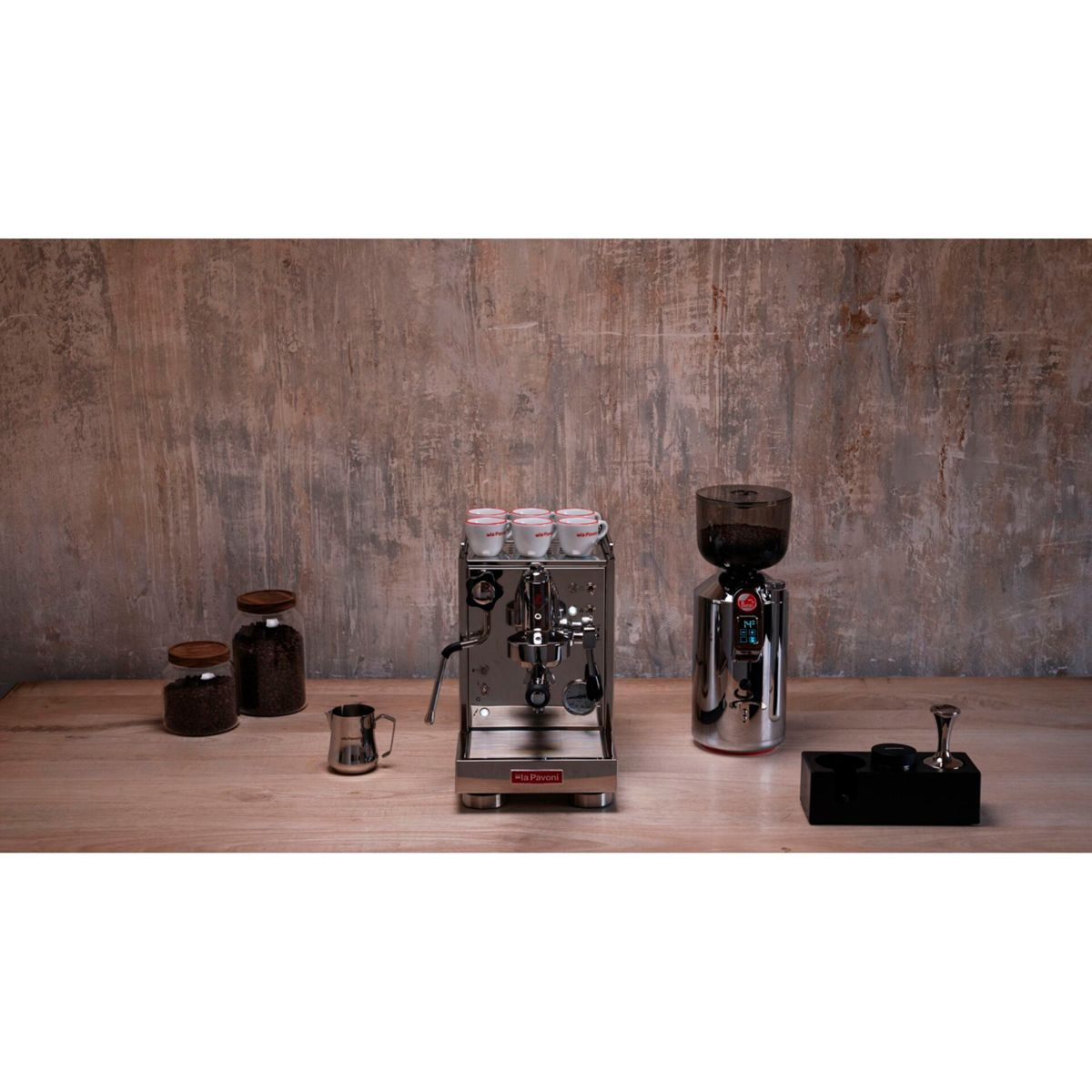 Espressomaschine mit Tassen, Kaffeemühle, Kannen und Tamper auf Holztisch.