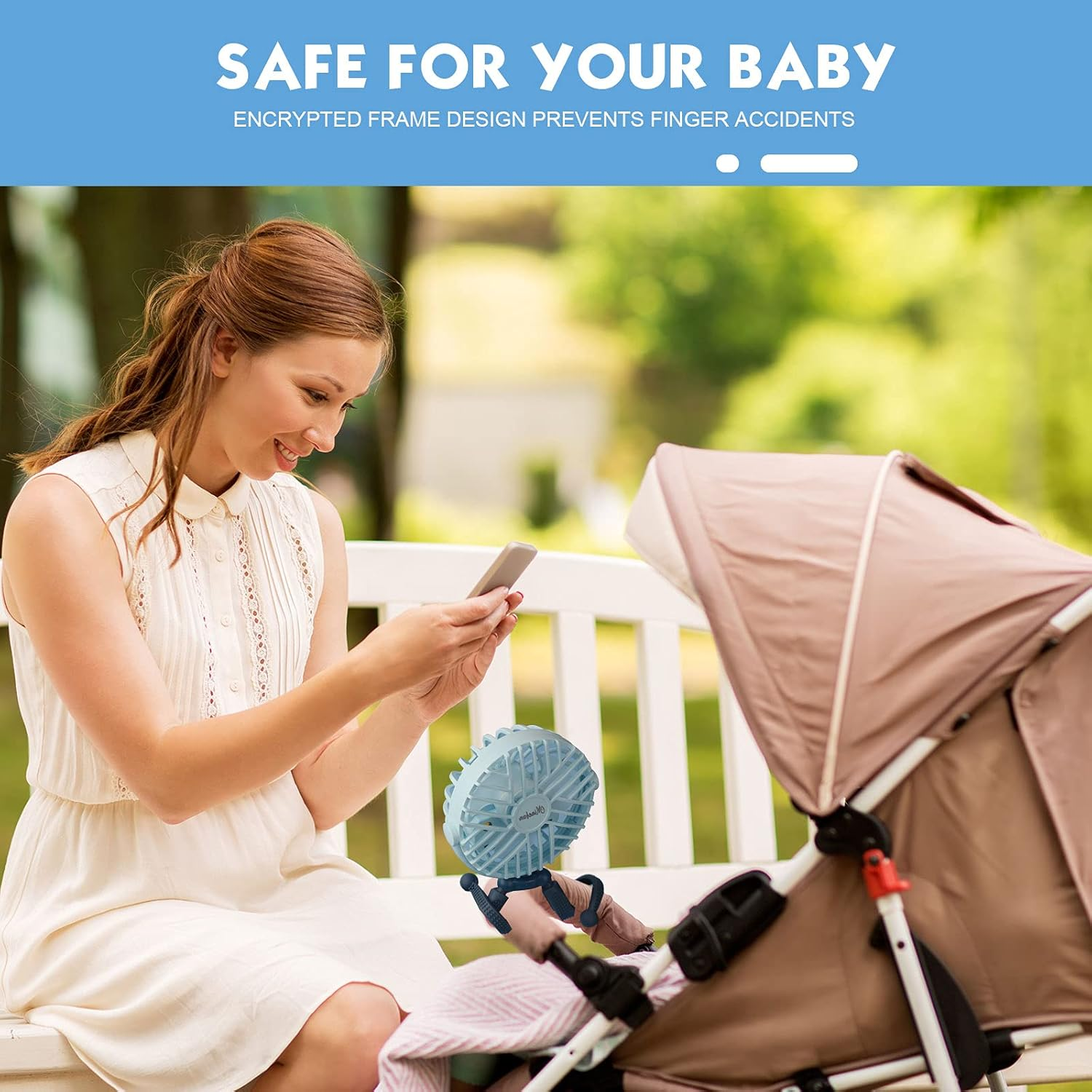 Eine Frau sitzt auf einer Bank und schaut auf ihr Handy. Ein kleiner Ventilator ist an einem Kinderwagen befestigt.