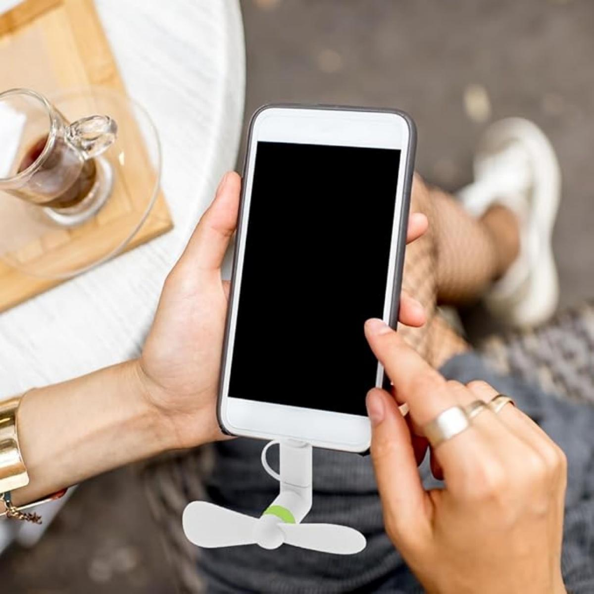 Eine Hand hält ein Smartphone mit einem kleinen weißen Ventilator am unteren Anschluss.