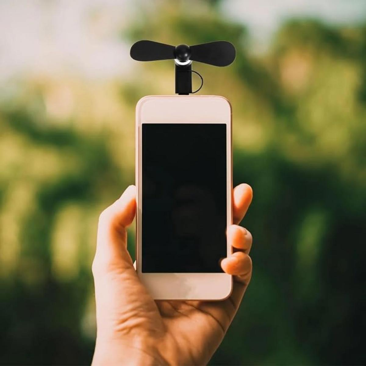 Eine Hand hält ein Smartphone mit einem kleinen schwarzen Ventilator, der an der Ladebuchse befestigt ist.