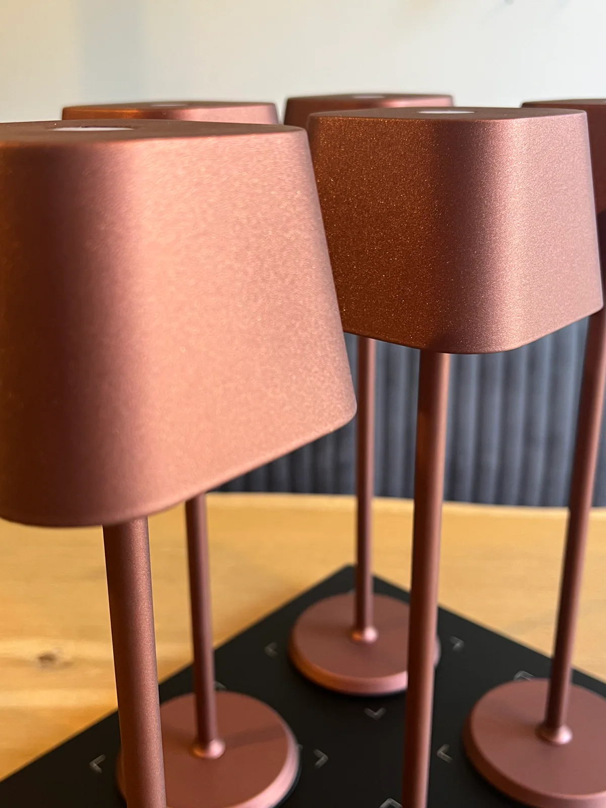 Vier kupferfarbene Tischlampen stehen auf einem schwarzen Sockel.