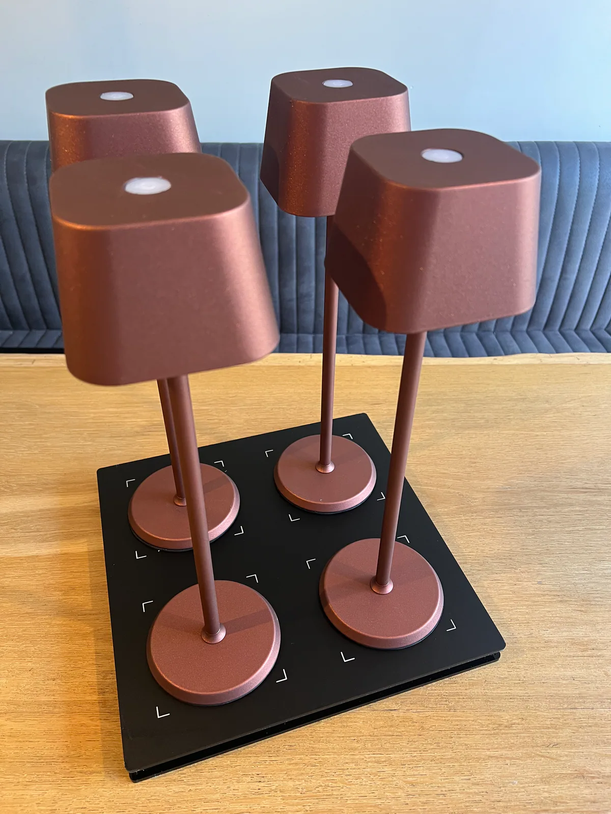 Vier kupferfarbene Tischlampen mit weißen Lichtern auf einer schwarzen Basis auf einem Holztisch.