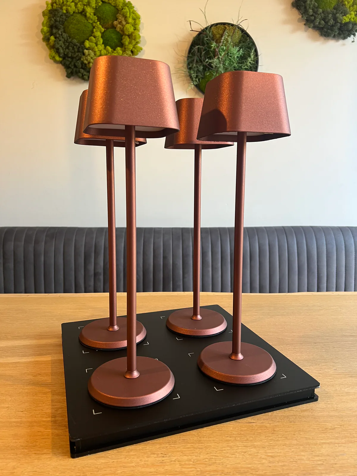 Vier kupferfarbene Tischlampen stehen auf einem schwarzen Ladegerät auf einem Holztisch.