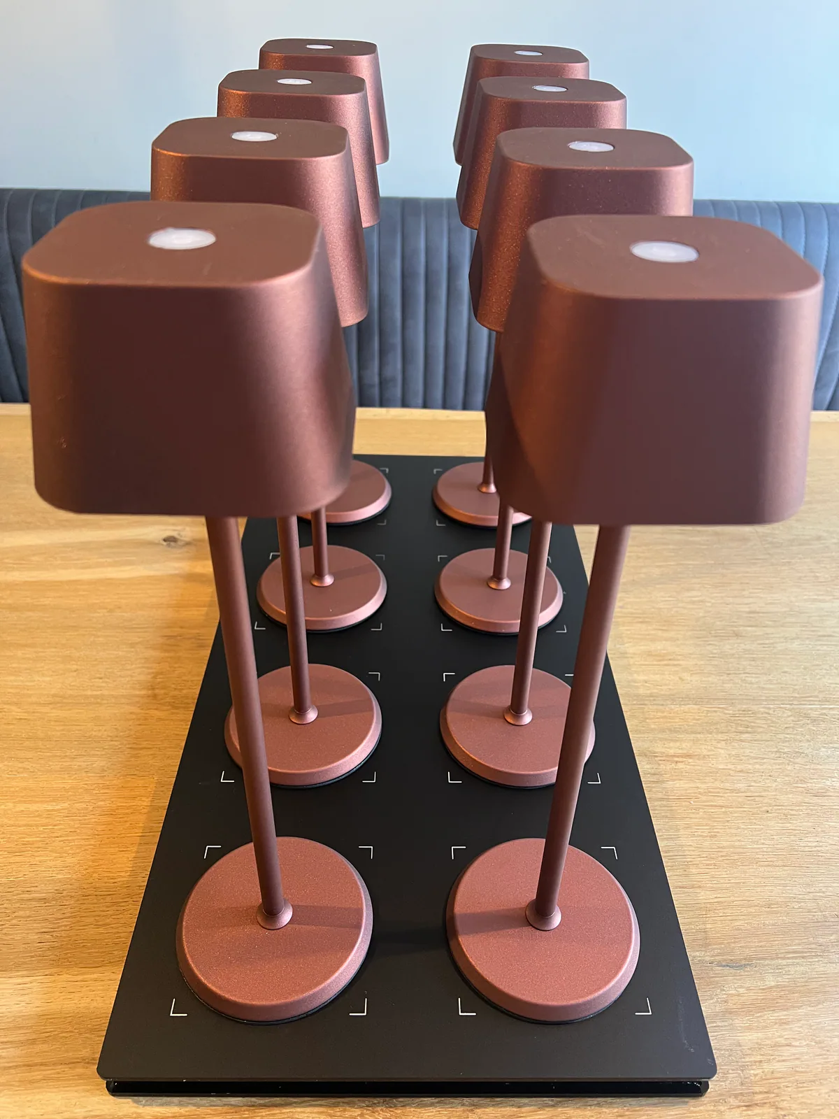 Acht kupferfarbene Tischlampen mit weißen Lichtern stehen auf einer schwarzen Ladestation.