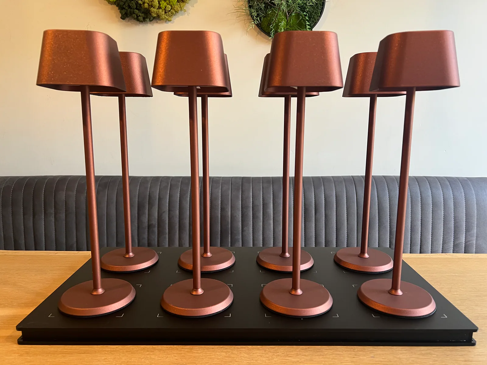 Acht bronzefarbene Tischlampen stehen auf einer schwarzen Ladestation.
