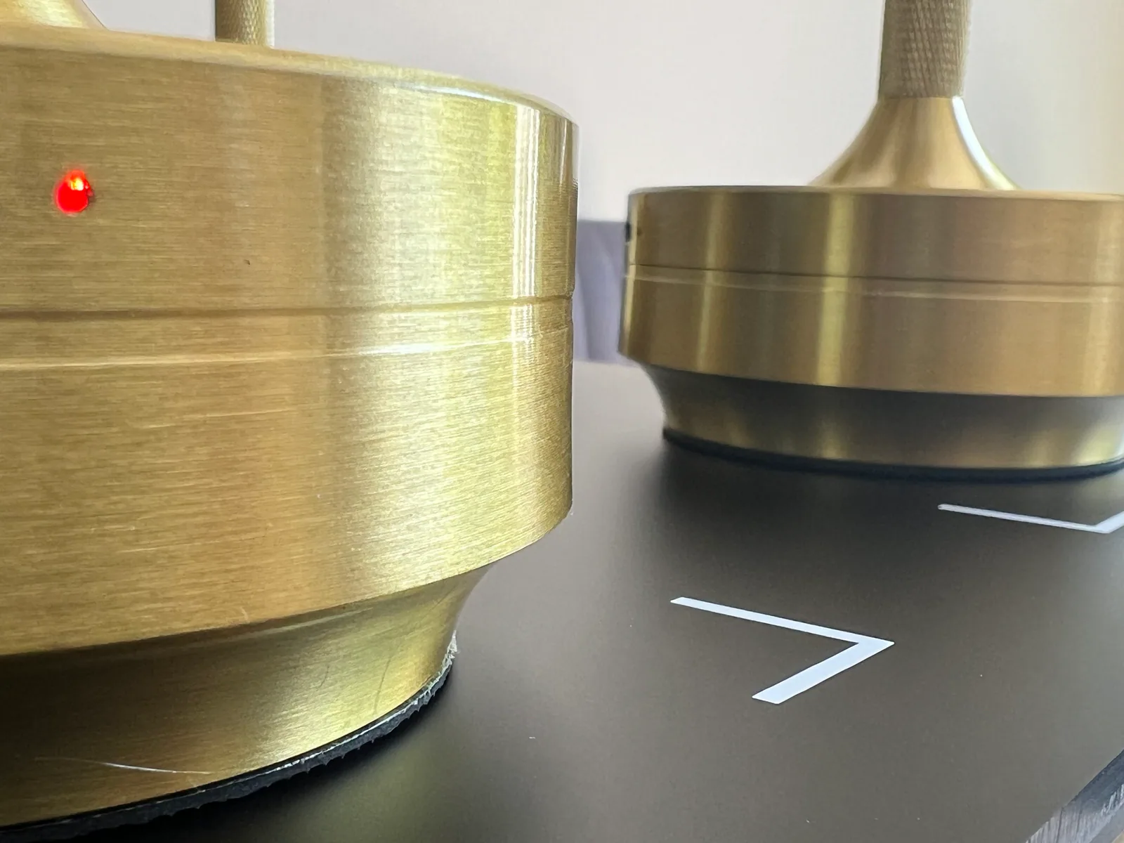 Zwei goldene Lampenfüße auf schwarzem Untergrund, eine mit roter LED.