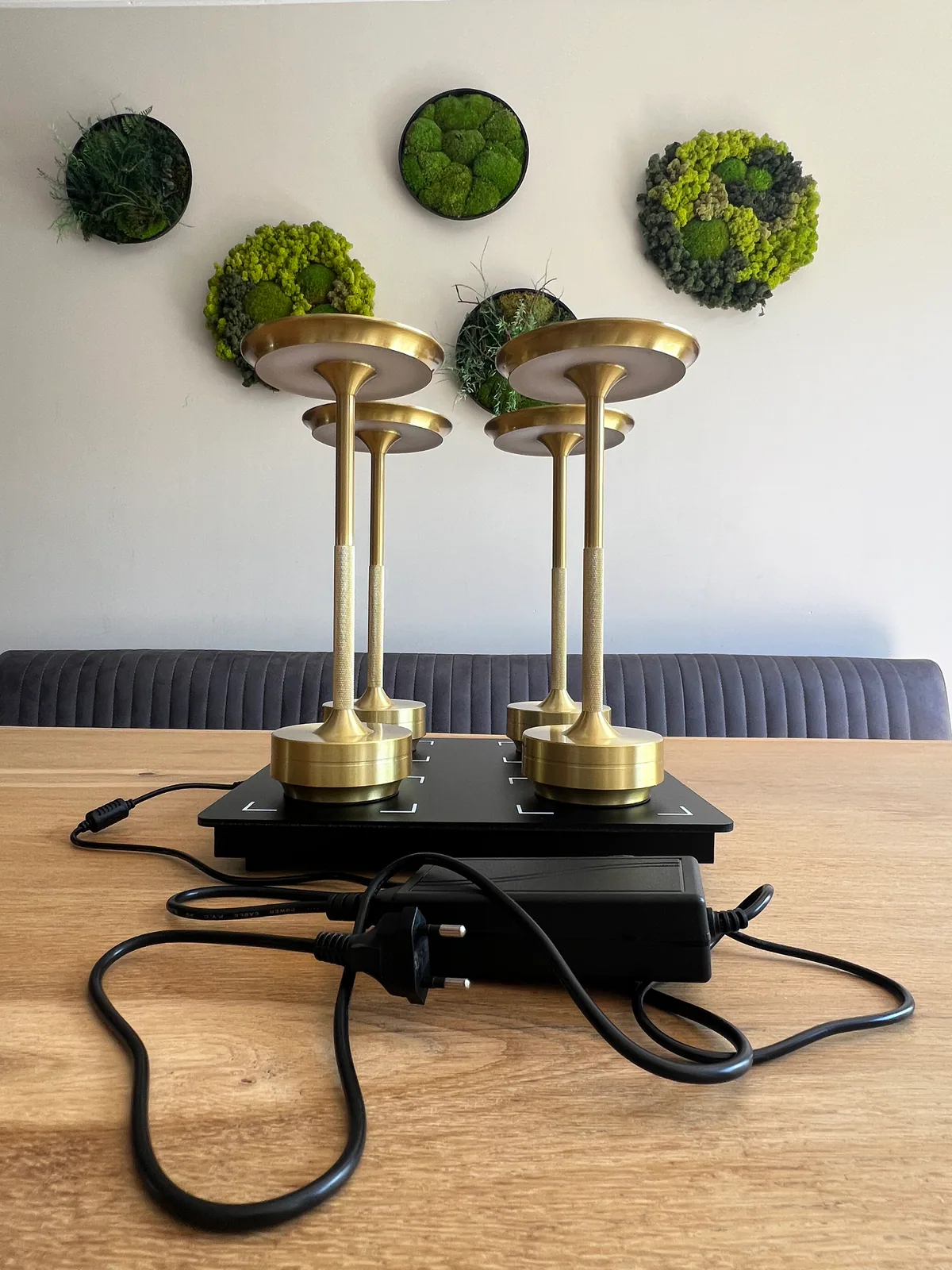 Vier goldene Lampen stehen auf einer schwarzen Ladestation auf einem Holztisch.