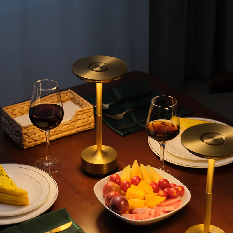 Zwei Weingläser, Obstschale, Tischtuch und Lampe auf einem Holztisch.