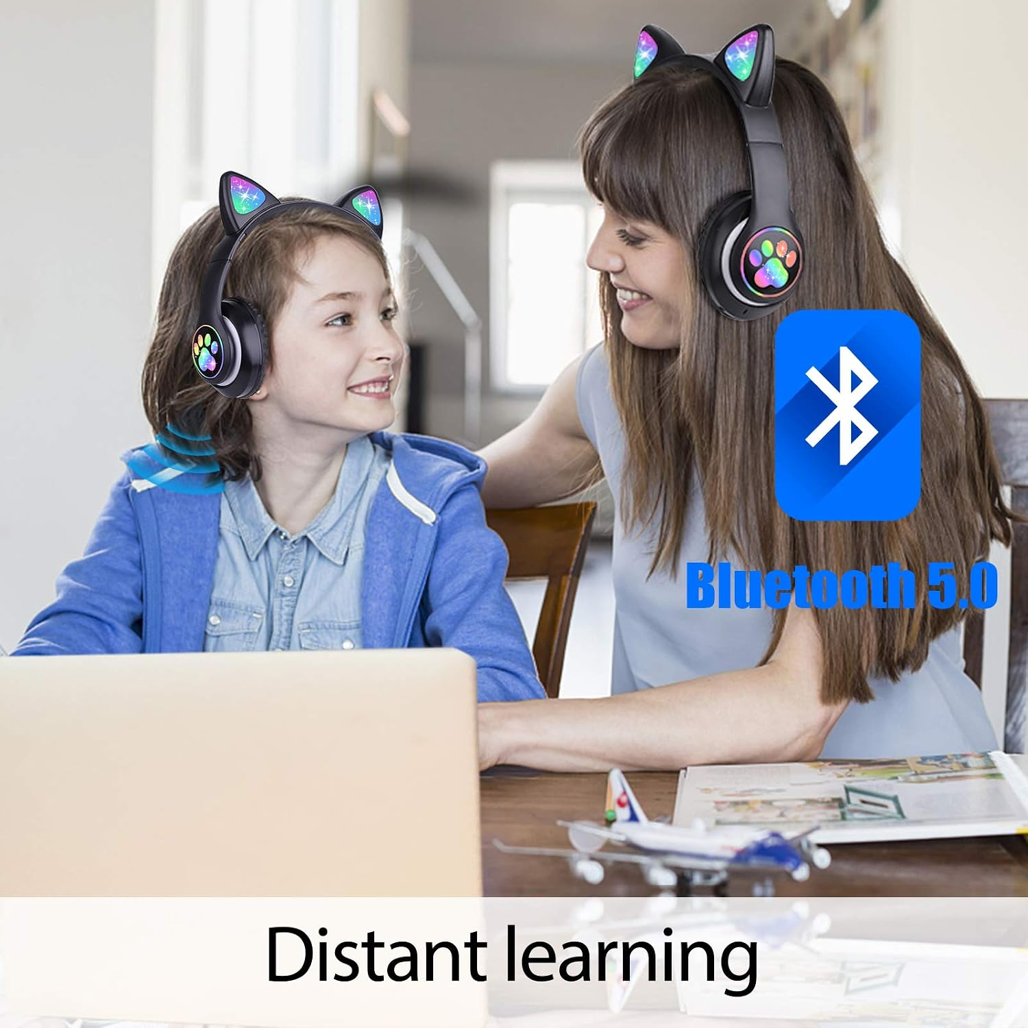 Frau und Kind mit Katzenohren-Kopfhörern am Tisch mit Laptop. Bluetooth 5.0.